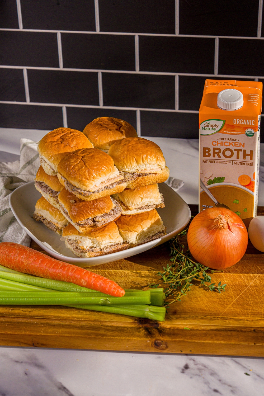 A wooden board with ingredients to make White Castle stuffing including White Castle sliders, chicken stock, egg, onion, celery, and carrots.
