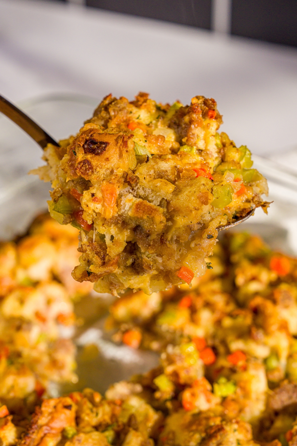 A close up of a large spoon with a scoop of White Castle stuffing. There is a baking dish of stuffing blurred in the background.