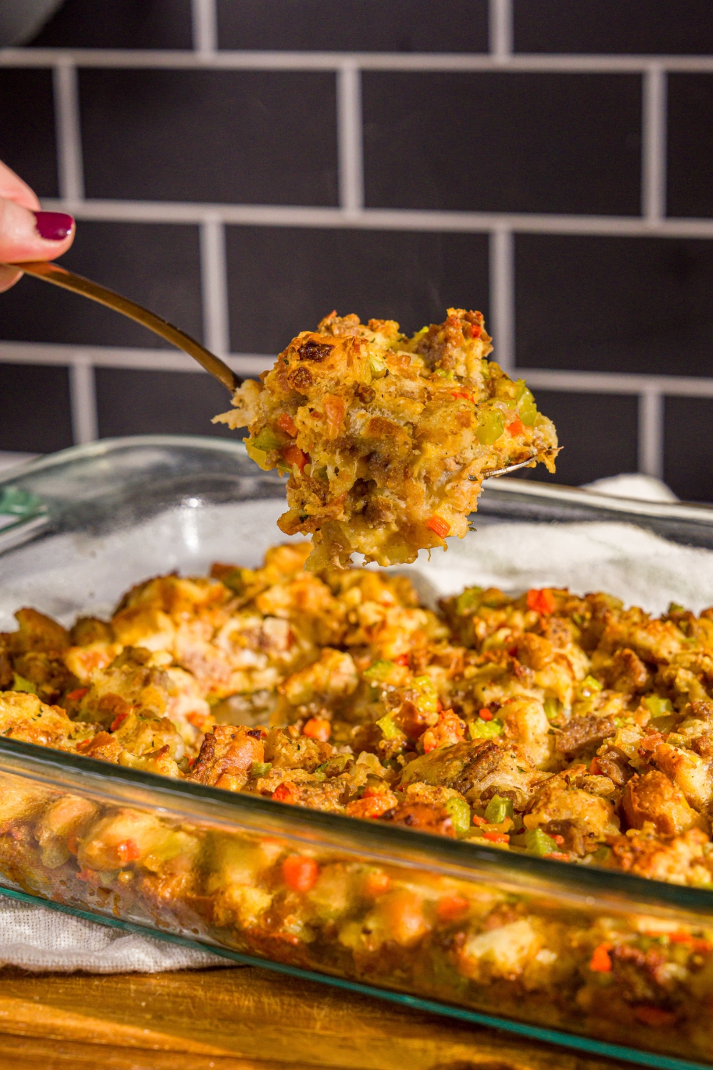 A baking dish of White Castle stuffing with a large spoon taking a scoop of stuffing from the dish. The dish is on a wooden board.