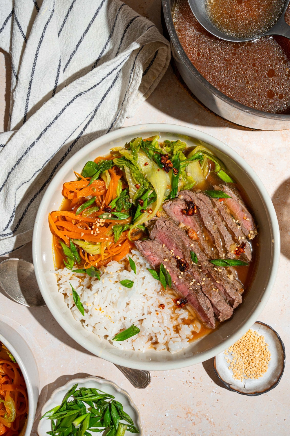 Sliced sirloin steak, shredded carrots and bok choy, and jasmine rice in a broth bowl.