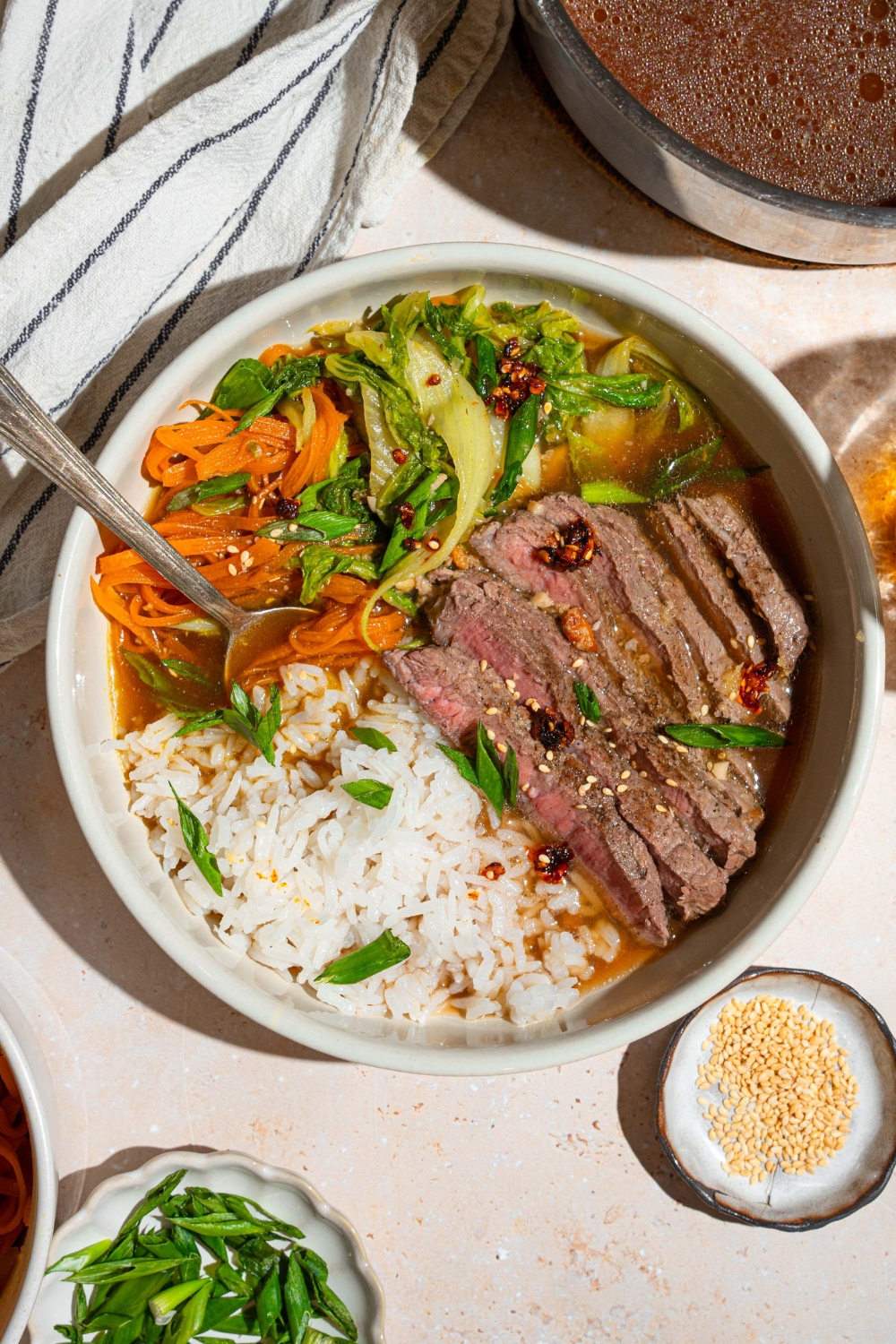 A brothy steak and rice bowl with sliced steak, shredded carrots and bok choy, and jasmine rice in broth in a white bowl.