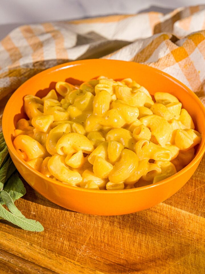 An orange bowl that is filled with butternut squash mac and cheese.