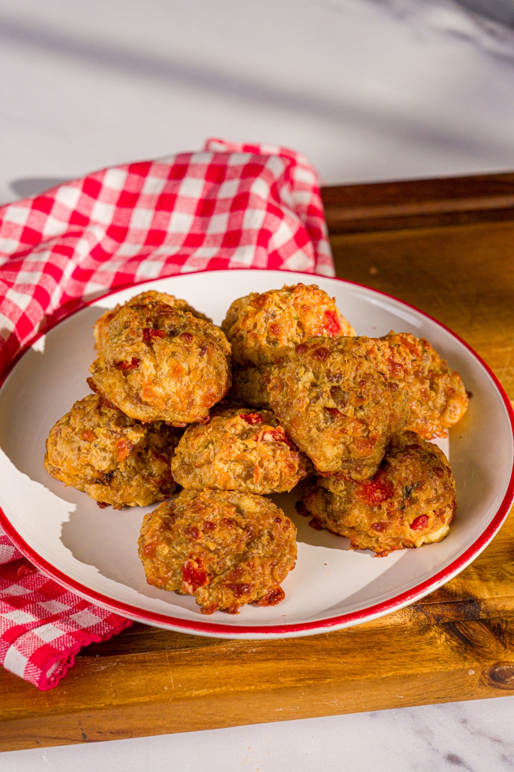 A plate of cheddar bay biscuit sausage balls. The plate is on a wooden board with a red checkered napkin.