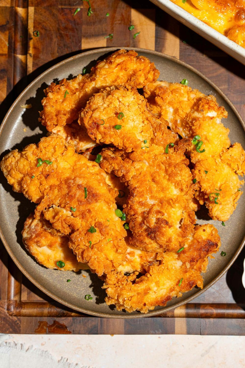 A green plate with copycat Chick-Fil-A tenders garnished with fresh parsley. The plate is on a wooden board with a baking dish of macaroni and cheese.