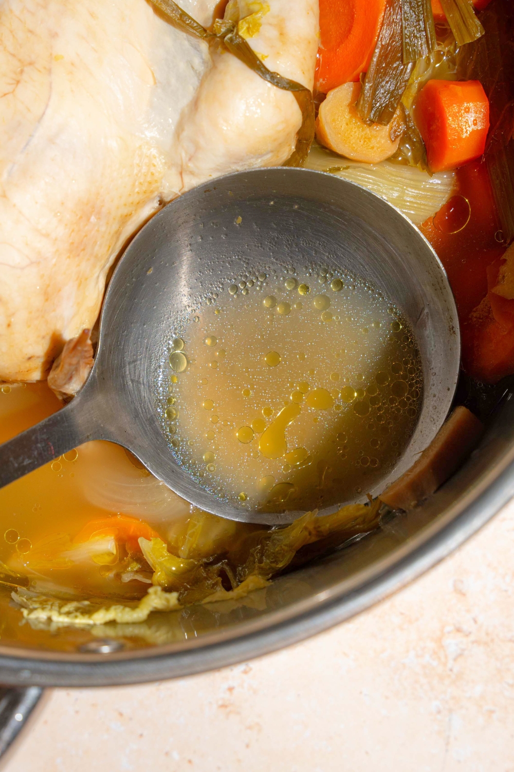 A spoon of broth being held in a pot that is filled with no water chicken soup.