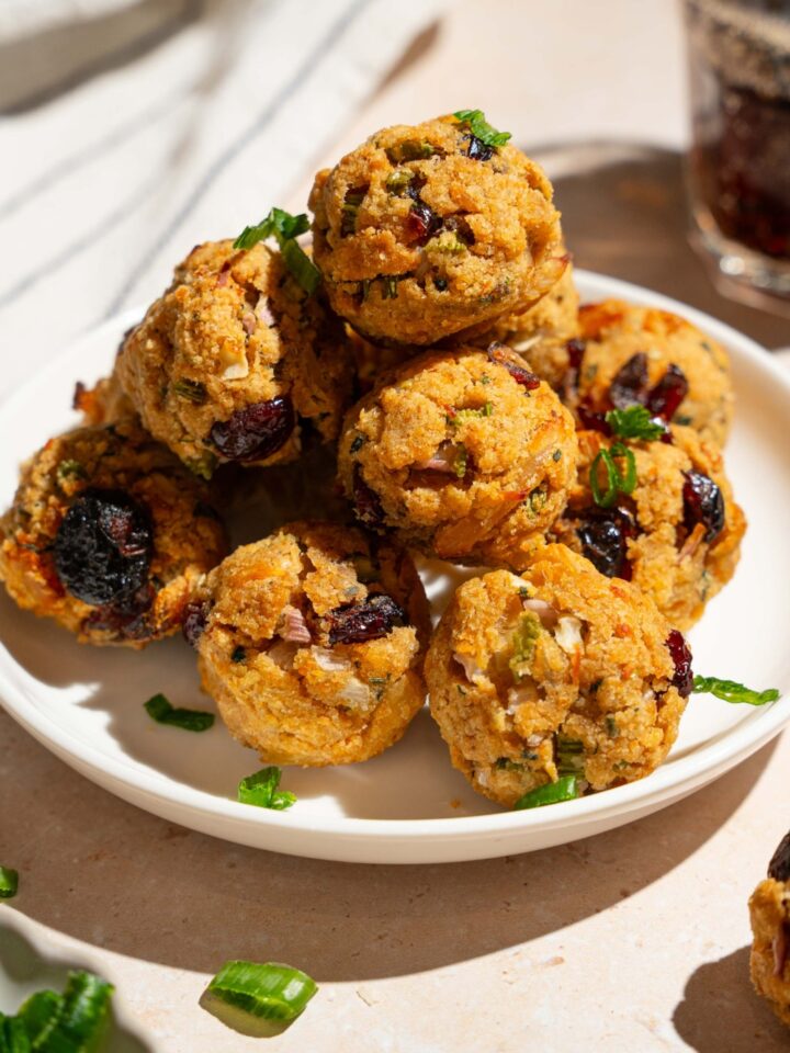 A white plate with cranberry turkey stuffing balls garnished with sliced green onions. The plate is on a tan counter with a white striped napkin.
