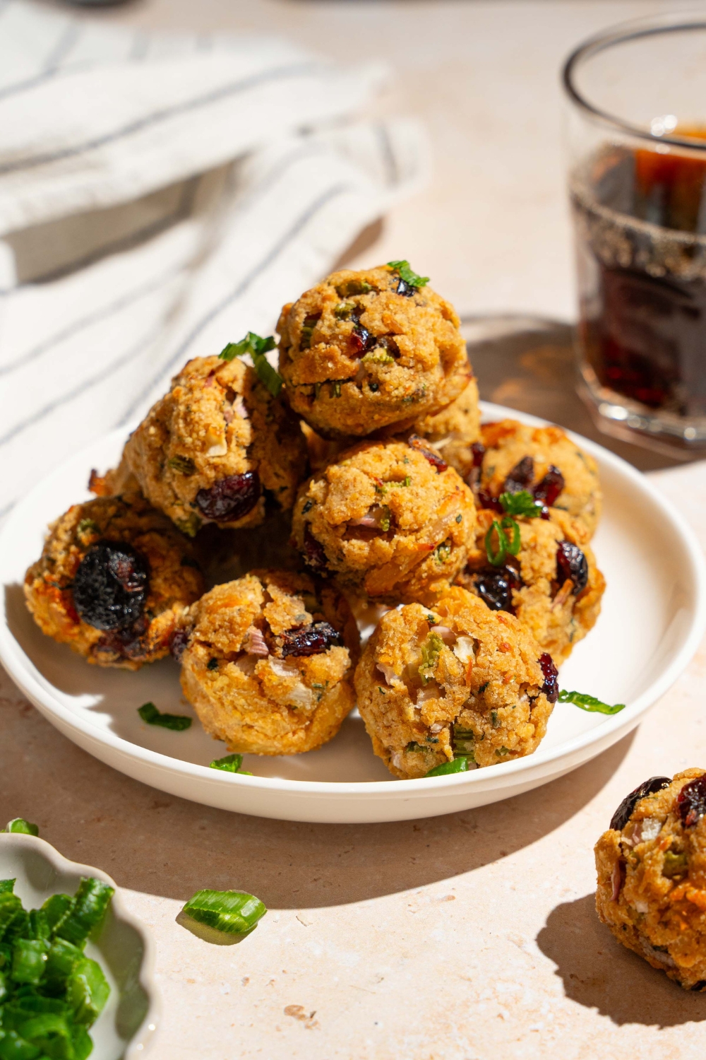 A white plate with cranberry turkey stuffing balls garnished with sliced green onions. The plate is on a tan counter with a white striped napkin.