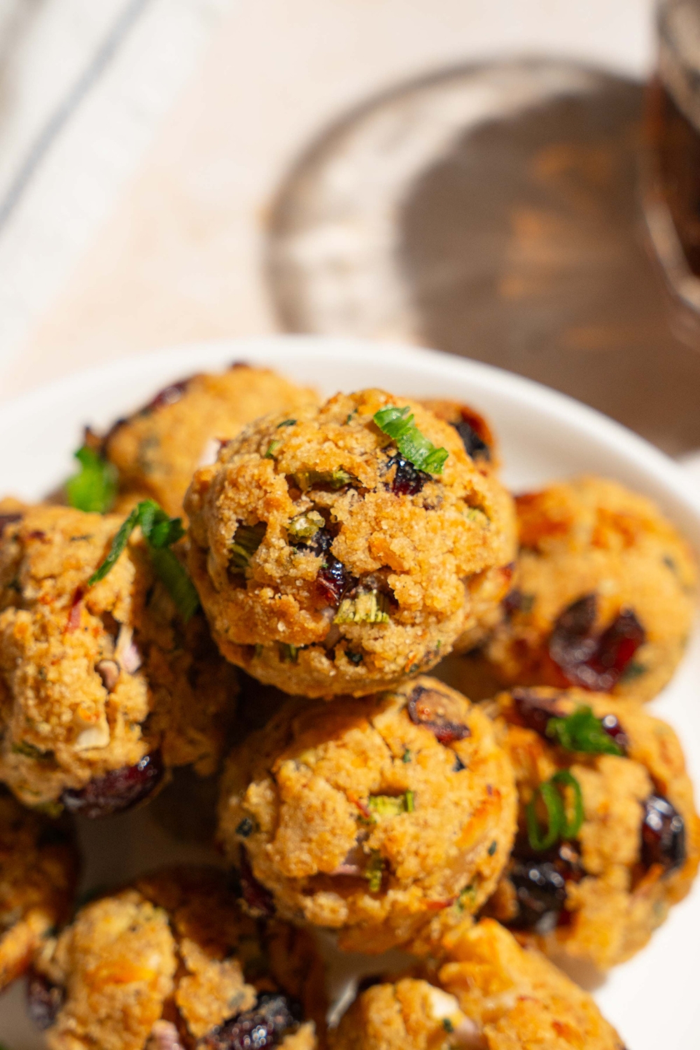 A white plate with cranberry turkey stuffing balls garnished with sliced green onions. The plate is on a tan counter.