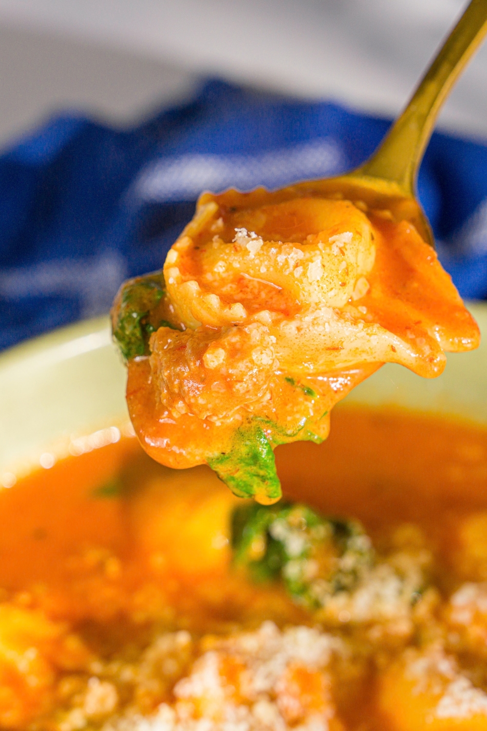 A close up of a spoon with a bite of creamy tomato tortellini soup. There is a bowl of soup blurred in the background.