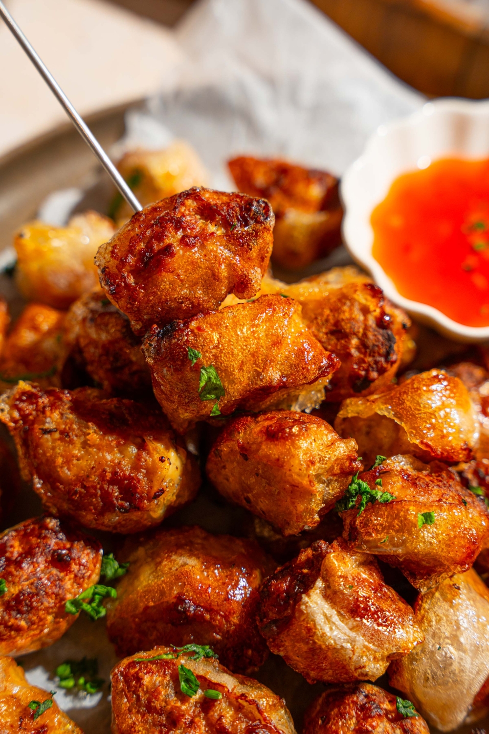 A skewer of crispy rice paper chicken bites on a plate of chicken bites. The plate is garnished with fresh parsley and served with a small bowl of dipping sauce.