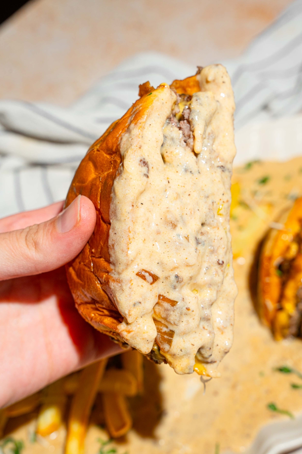 A hand holding half of a cheeseburger with the inside of it covered with a creamy garlic Parmesan sauce.