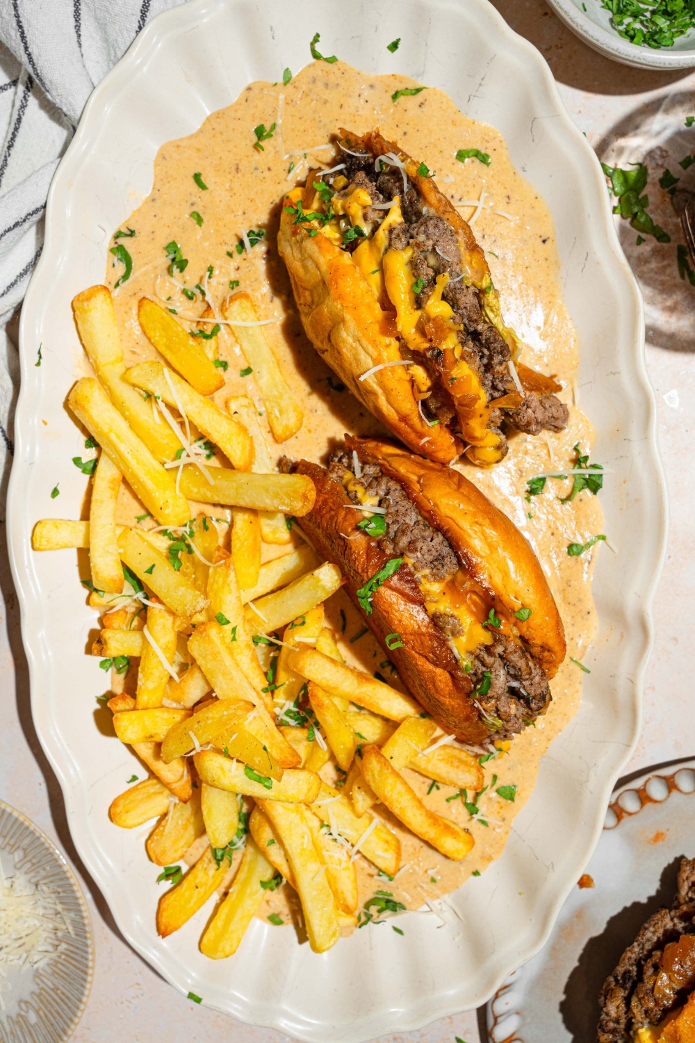 A cheeseburger that is cut in half with the inside face down in a creamy garlic Parmesan sauce with french fries next to it on a white serving tray.