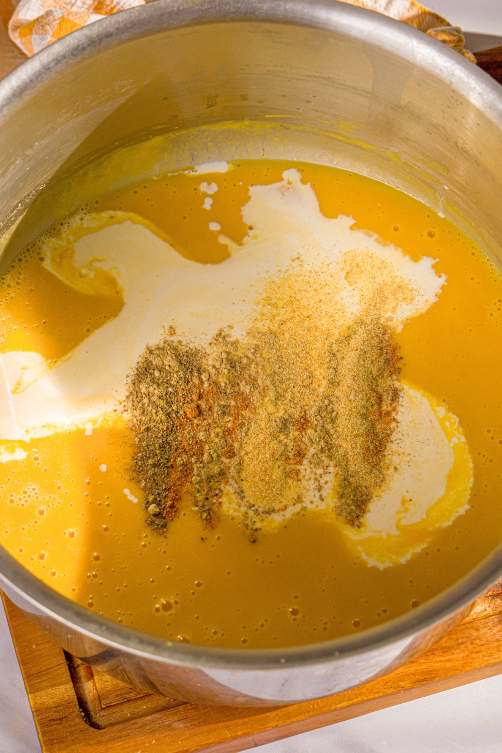 A large pot with nutmeg, sage, garlic powder, black pepper, and heavy cream on top of pureed roasted butternut squash.