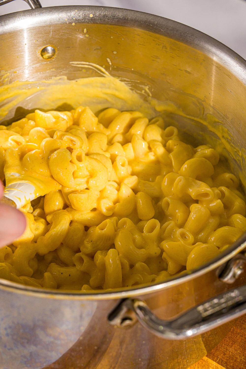 A large pot that is filled with butternut squash mac and cheese being mixed my a hand holding a rubber spatula.