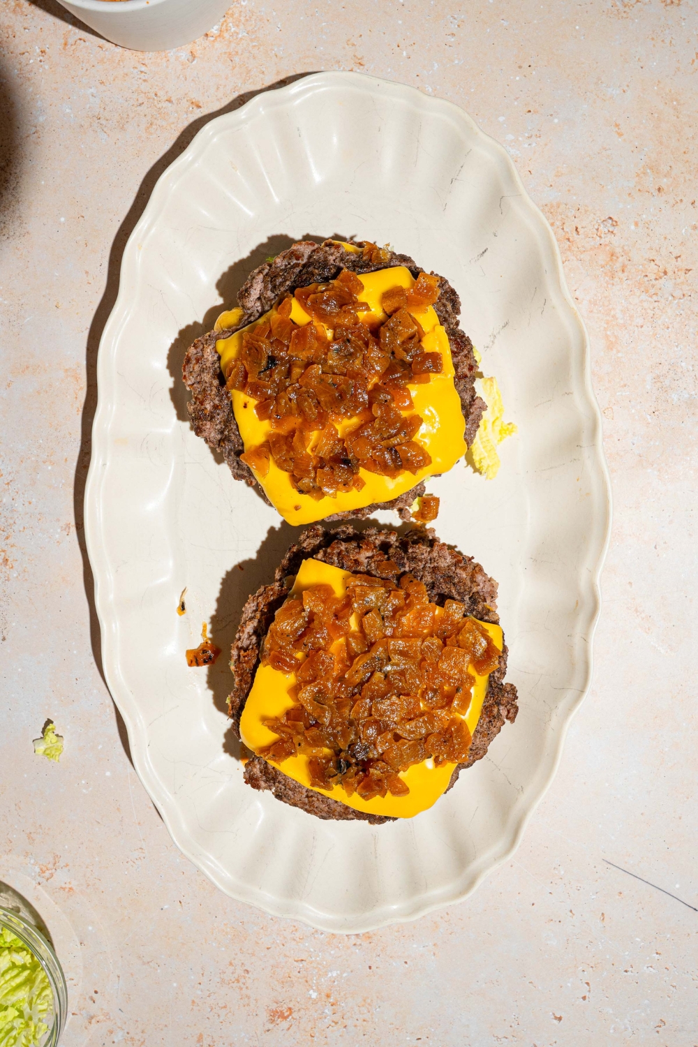 Two burger patties on a white serving tray with a slice of American cheese and caramelized onions on top.