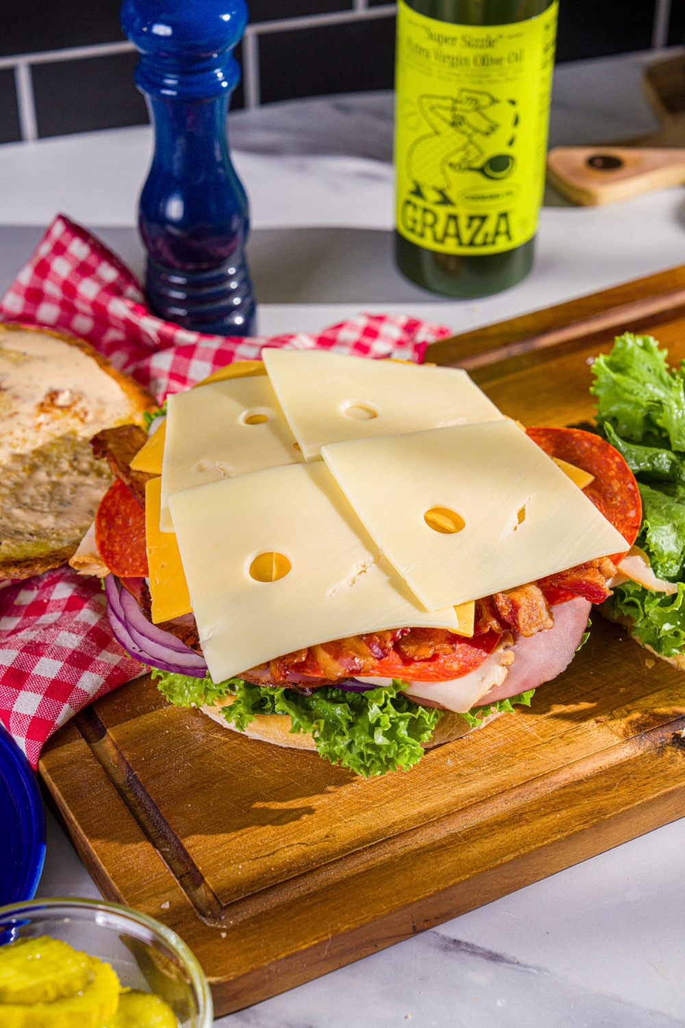 Swiss cheese on top of slices of cheddar cheese on top of lettuce, tomato, and onion that is on deli meats on a slice of bread.