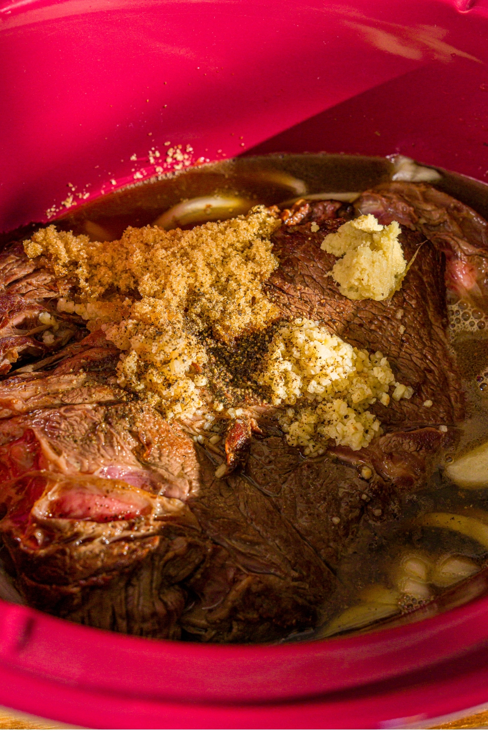 Minced garlic, grated ginger, and brown sugar on top of seared chuck roast in a sauce in a crock pot.