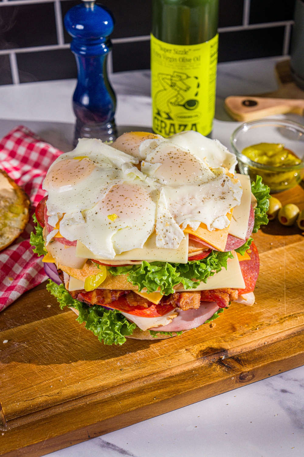 Sunny side up eggs on top of swiss and american cheese, lettuce, tomato, onion, deli meats, a slice of bread, then more swiss and american cheese, lettuce, tomato, onion, and deli meats.