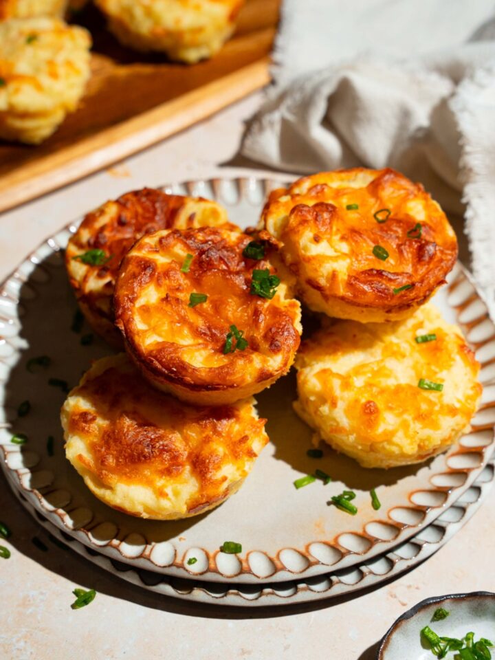 A plate with several mashed potato cups garnished with sliced green onion. The plate is on a tan counter with a small plate of garnishes.