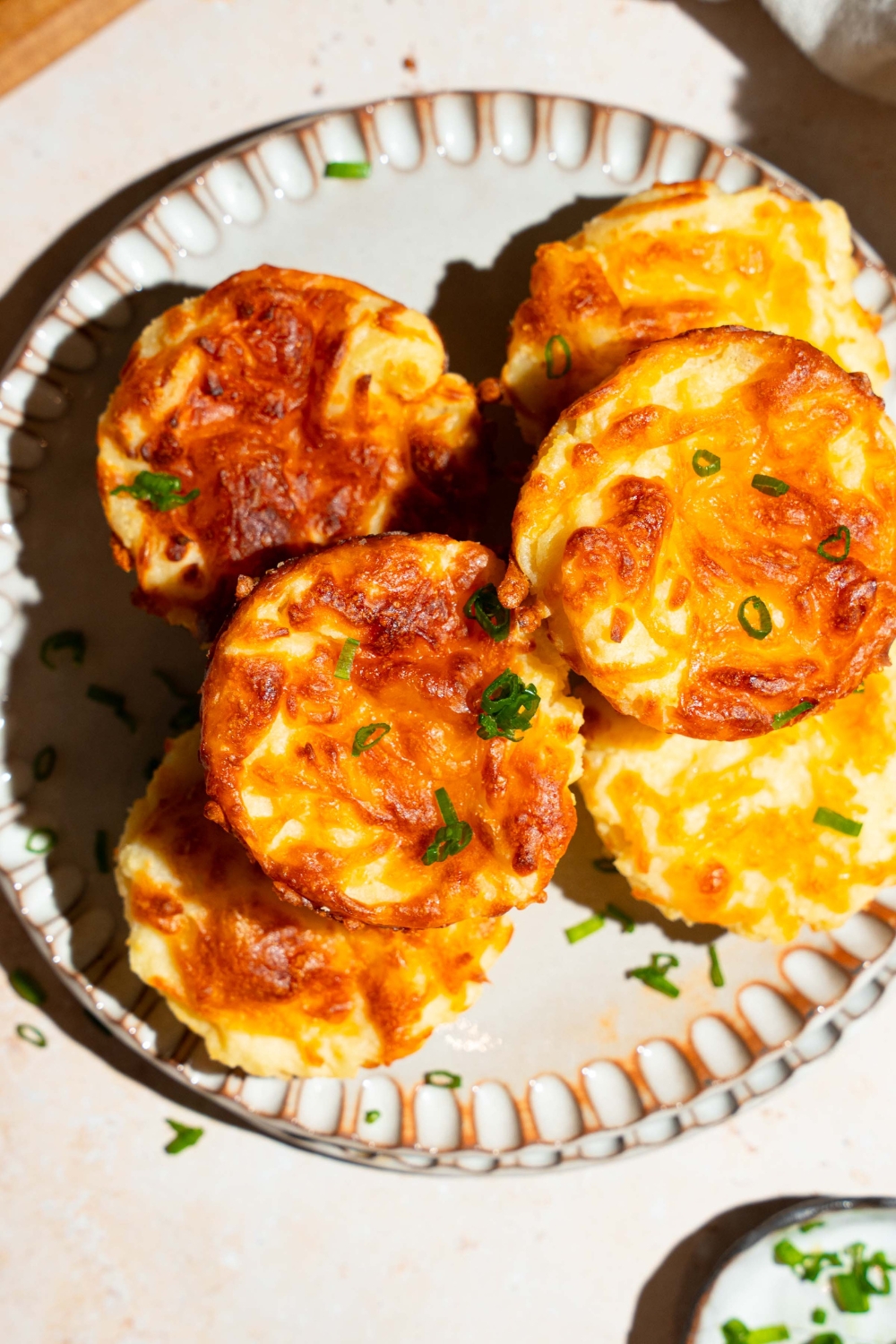 A plate with several mashed potato cups garnished with sliced green onion. The plate is on a tan counter with a small plate of garnishes.
