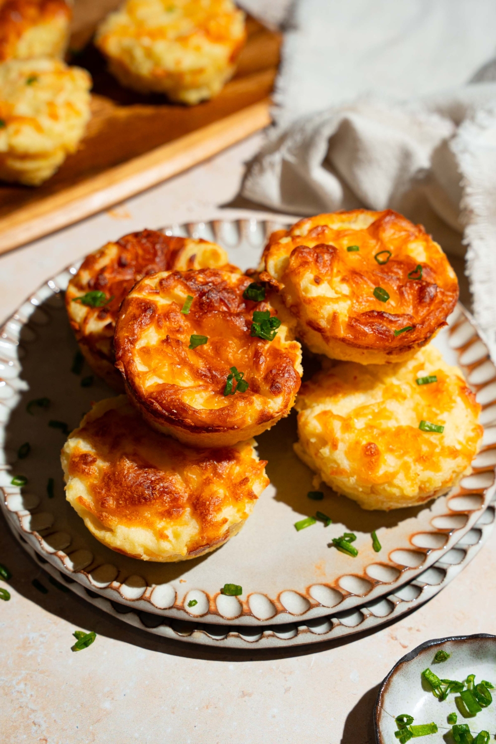 A plate with several mashed potato cups garnished with sliced green onion. The plate is on a tan counter with a small plate of garnishes.