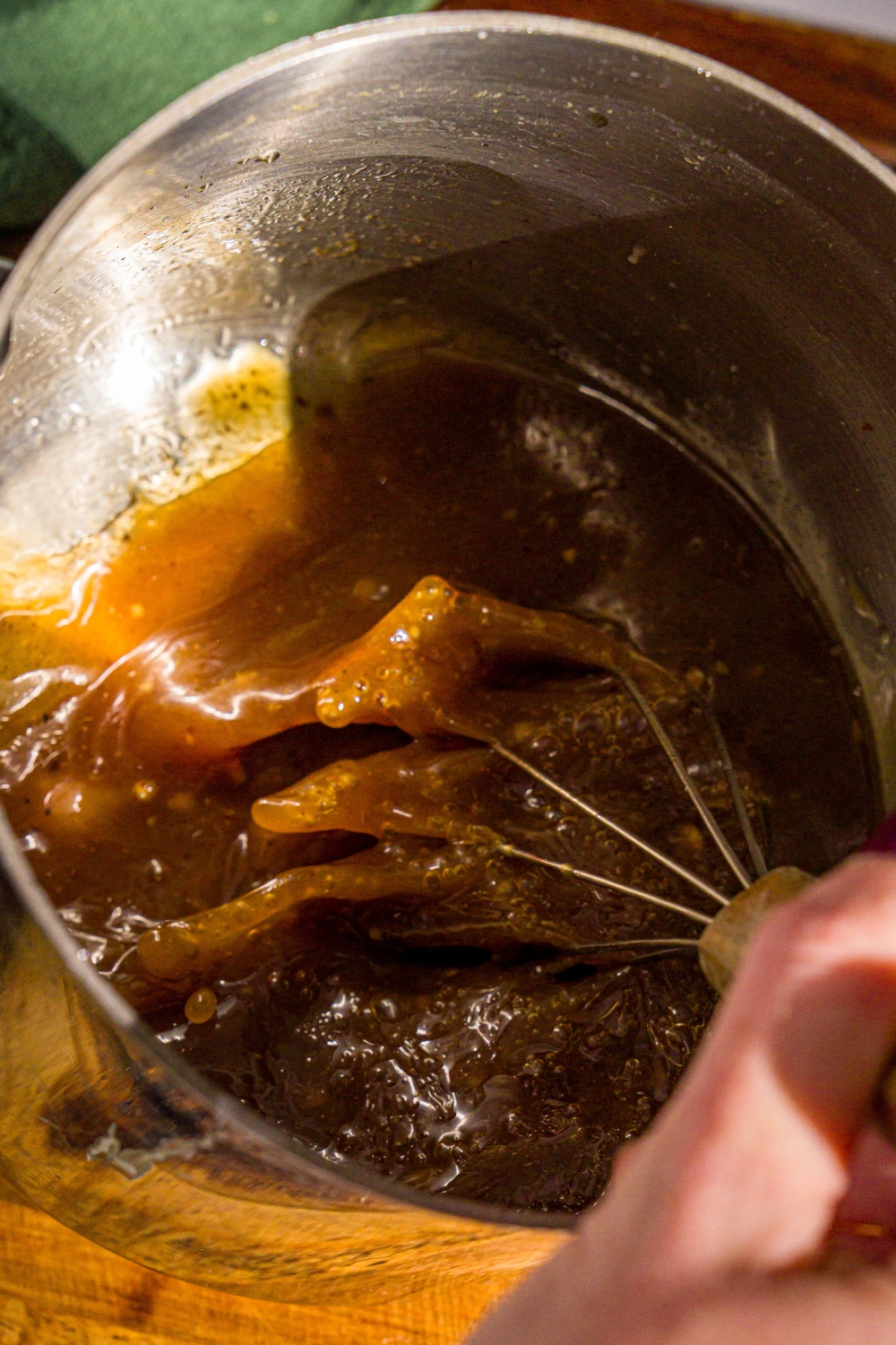 A hand whisking a sauce in a large pot for mongolian beef.