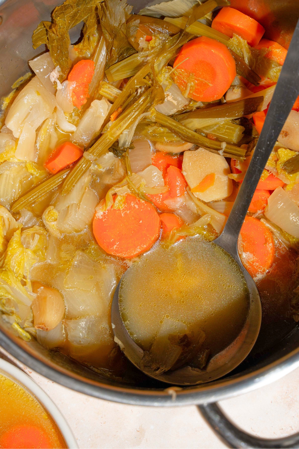 Part of a pot of cooked no water chicken soup consisting of sliced carrots, scallions, celery, and garlic.