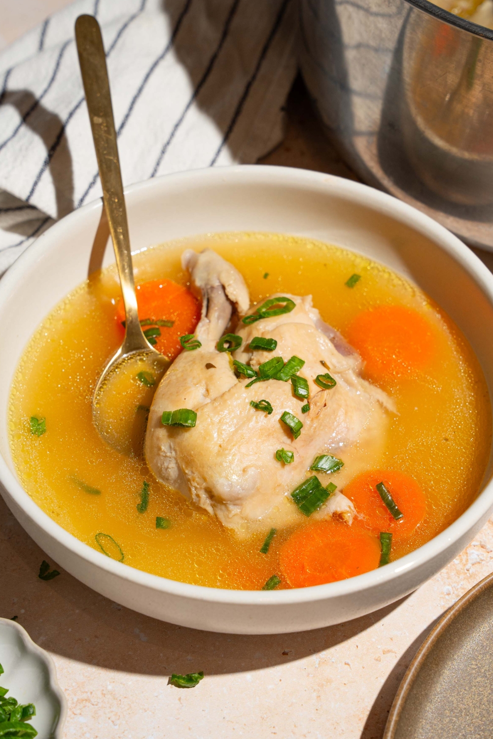 A bowl that is filled with no water chicken soup consisting of part of the chicken and some carrot slices.