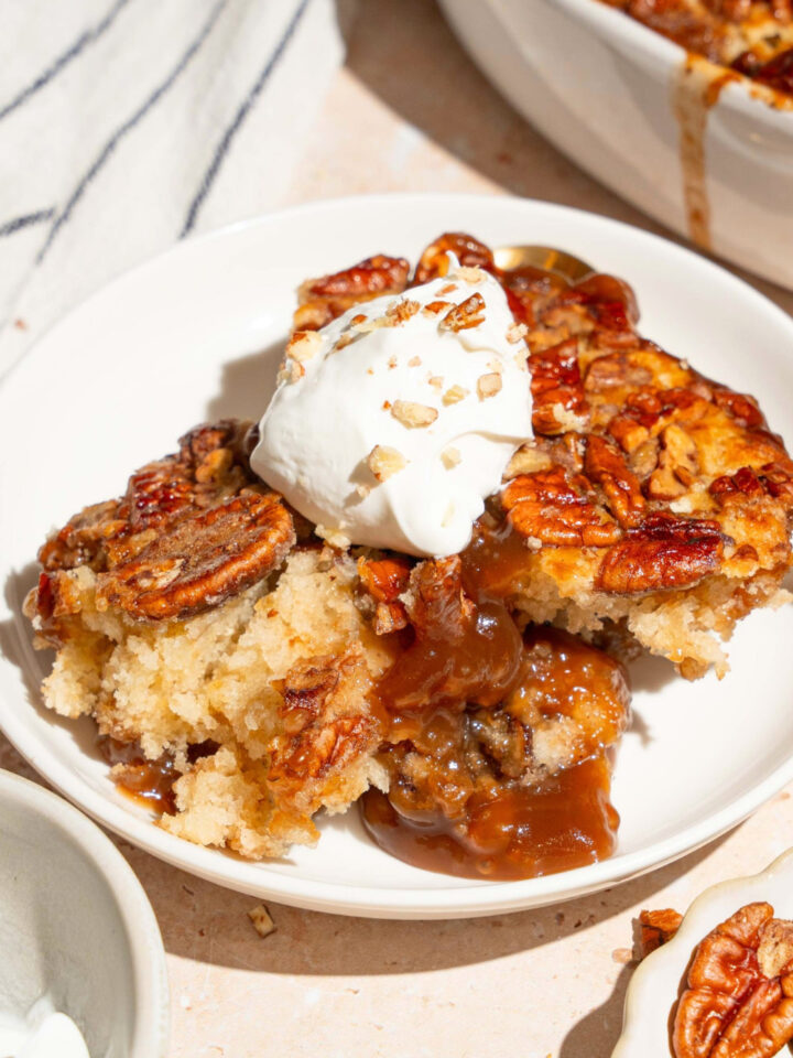 A large scoop of pecan pie cobbler with a small scoop of vanilla ice cream on top on a white plate.