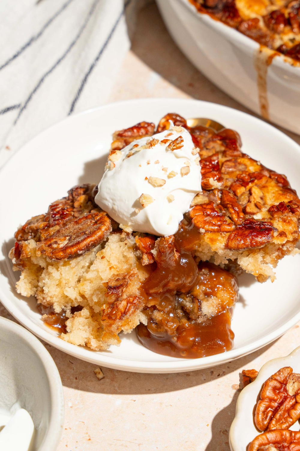 A large scoop of pecan pie cobbler with a small scoop of vanilla ice cream on top on a white plate.
