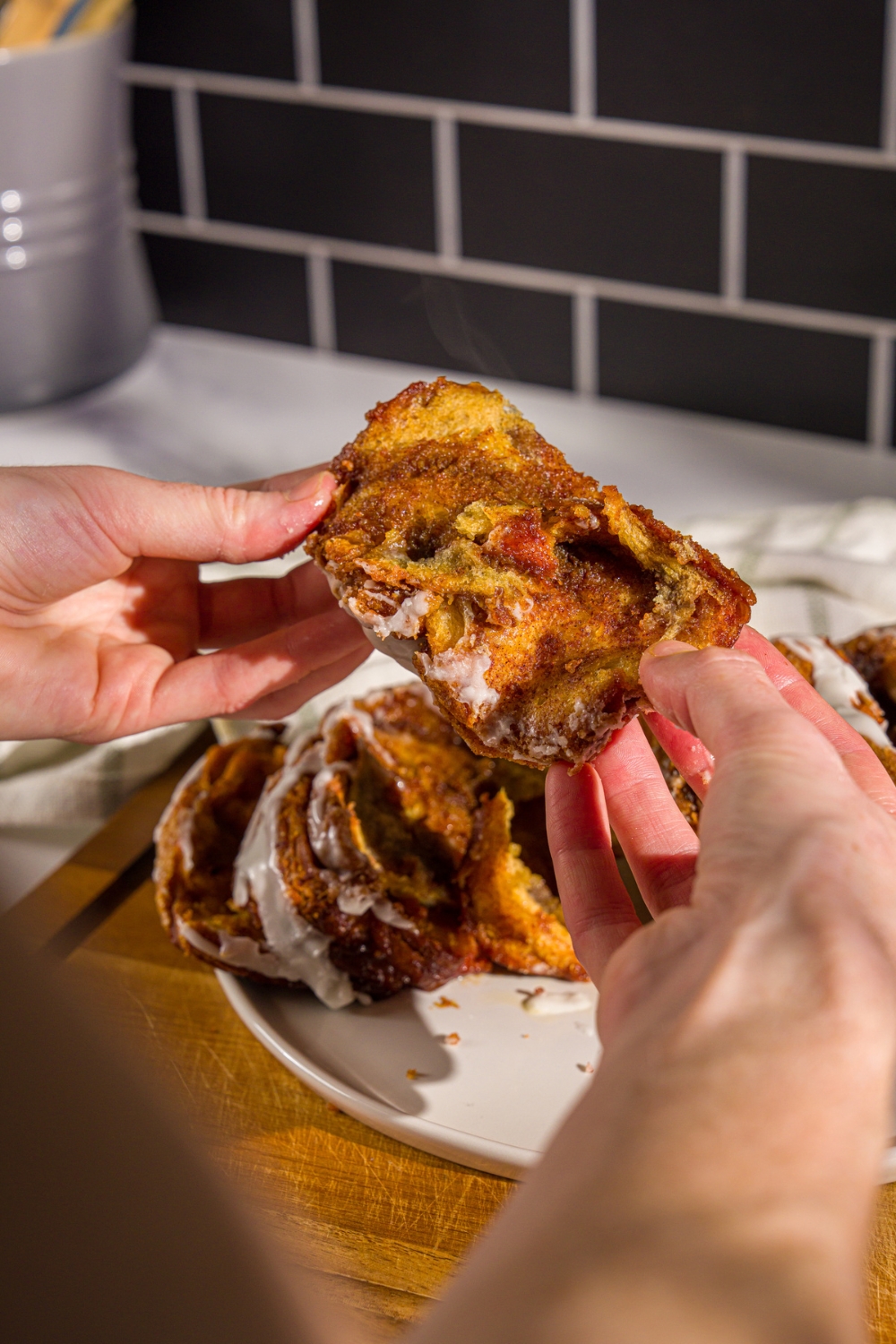 A pair of hands holding a slice of pumpkin pull apart bread. There is a plate of pumpkin bread on a wooden board in the background.