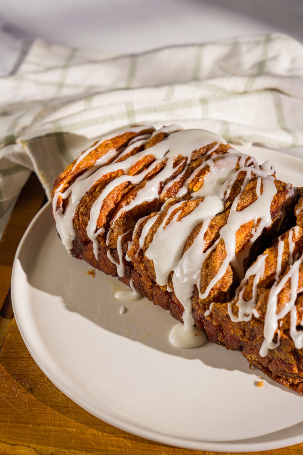 A plate of pumpkin pull apart bread loaf drizzled with glaze. The plate is on a wooden board with a white cloth napkin.