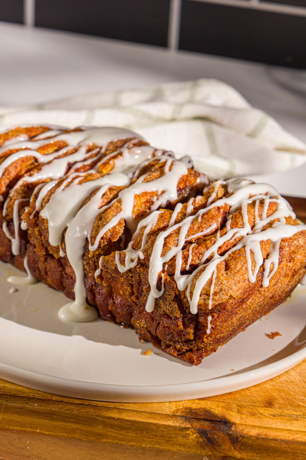 A plate of pumpkin pull apart bread loaf drizzled with glaze. The plate is on a wooden board with a white cloth napkin.