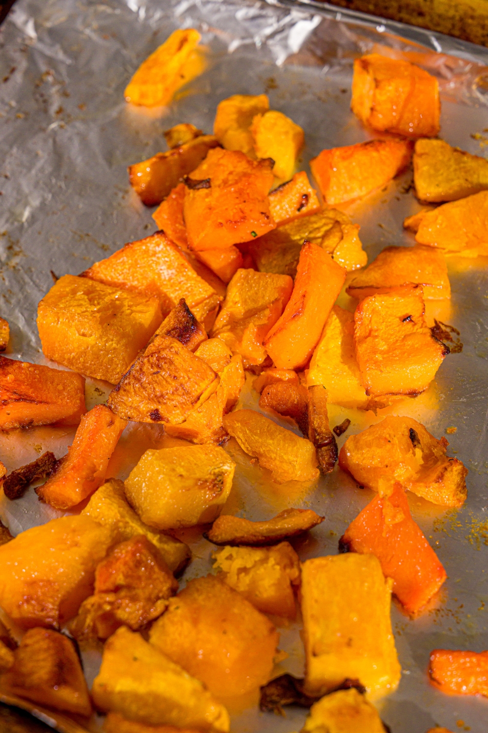 A bunch of cubed roasted butternut squash on a foil lined baking sheet.