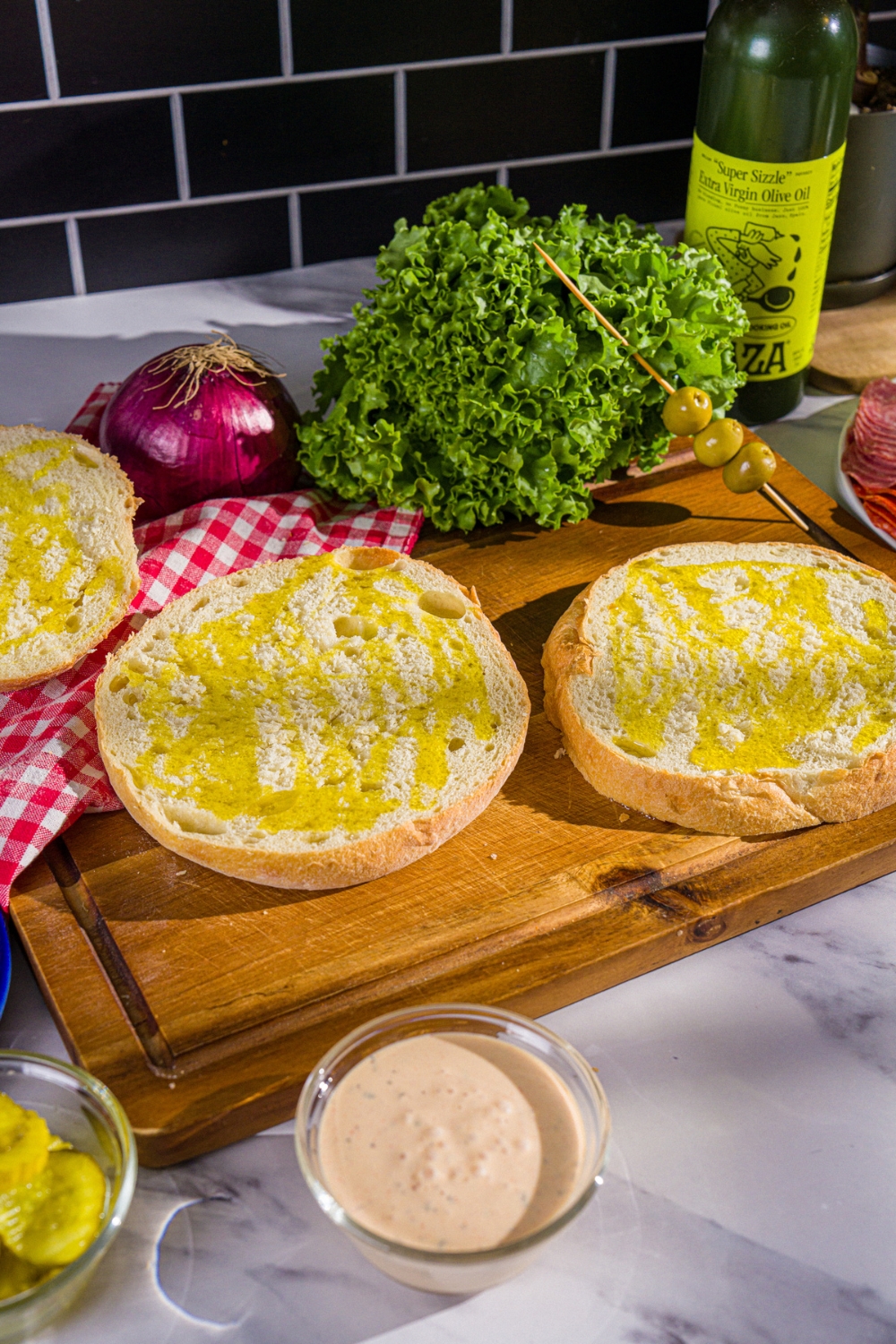 Two rounds of Italian bread face up with olive oil spread on them on a wood cutting board.