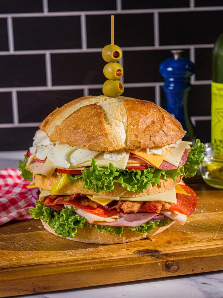 An assembled scooby doo sandwich consisting of three layers of swiss and american cheese, lettuce, tomato, onion, and deli meats.