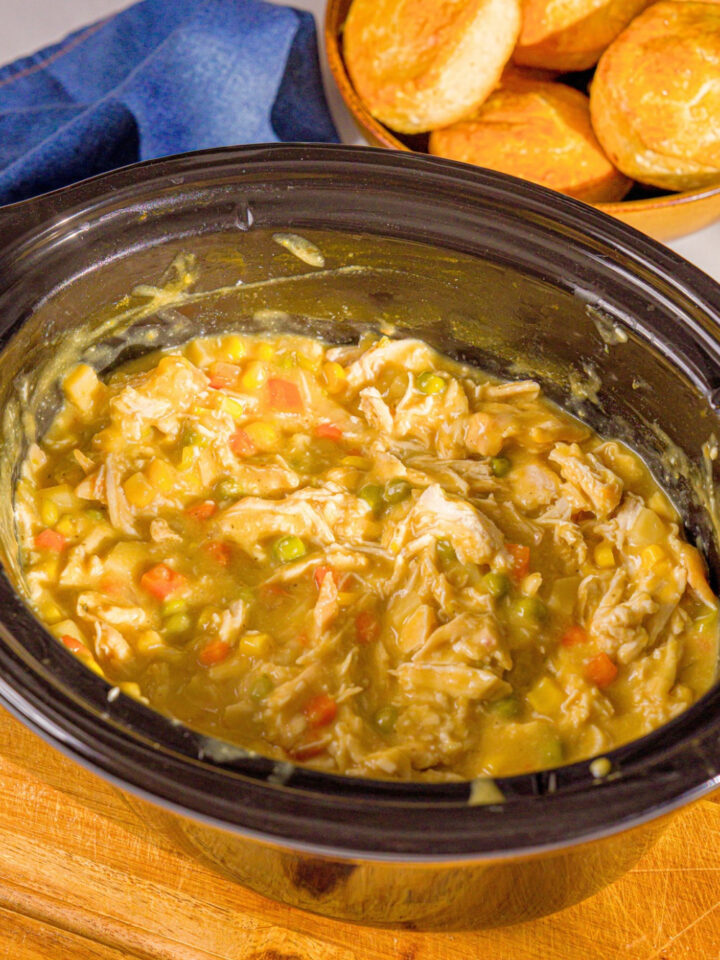 Shredded chicken, diced carrots and potatoes, and peas in a creamy sauce cooking in a black crock pot.