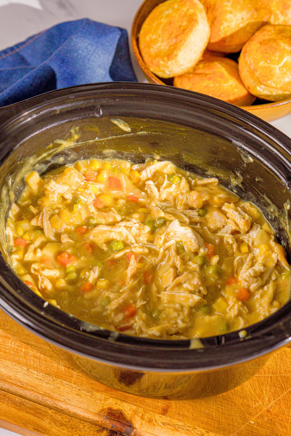Shredded chicken, diced carrots and potatoes, and peas in a creamy sauce cooking in a black crock pot.