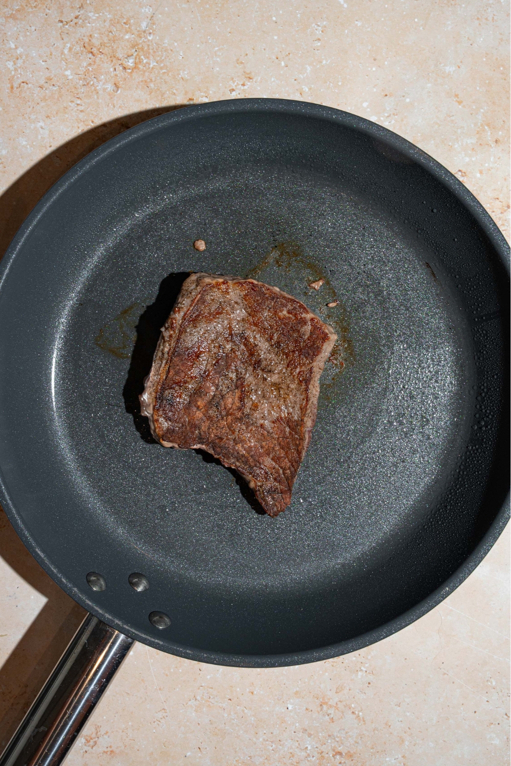 A sirloin steak cooking in a large skillet.
