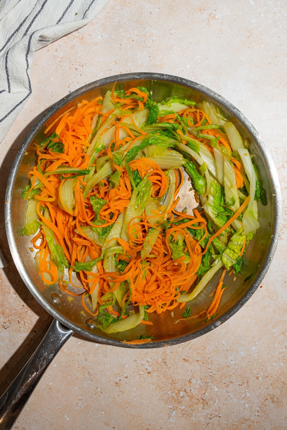 Shredded carrots and bok choy cooking in a large skillet.