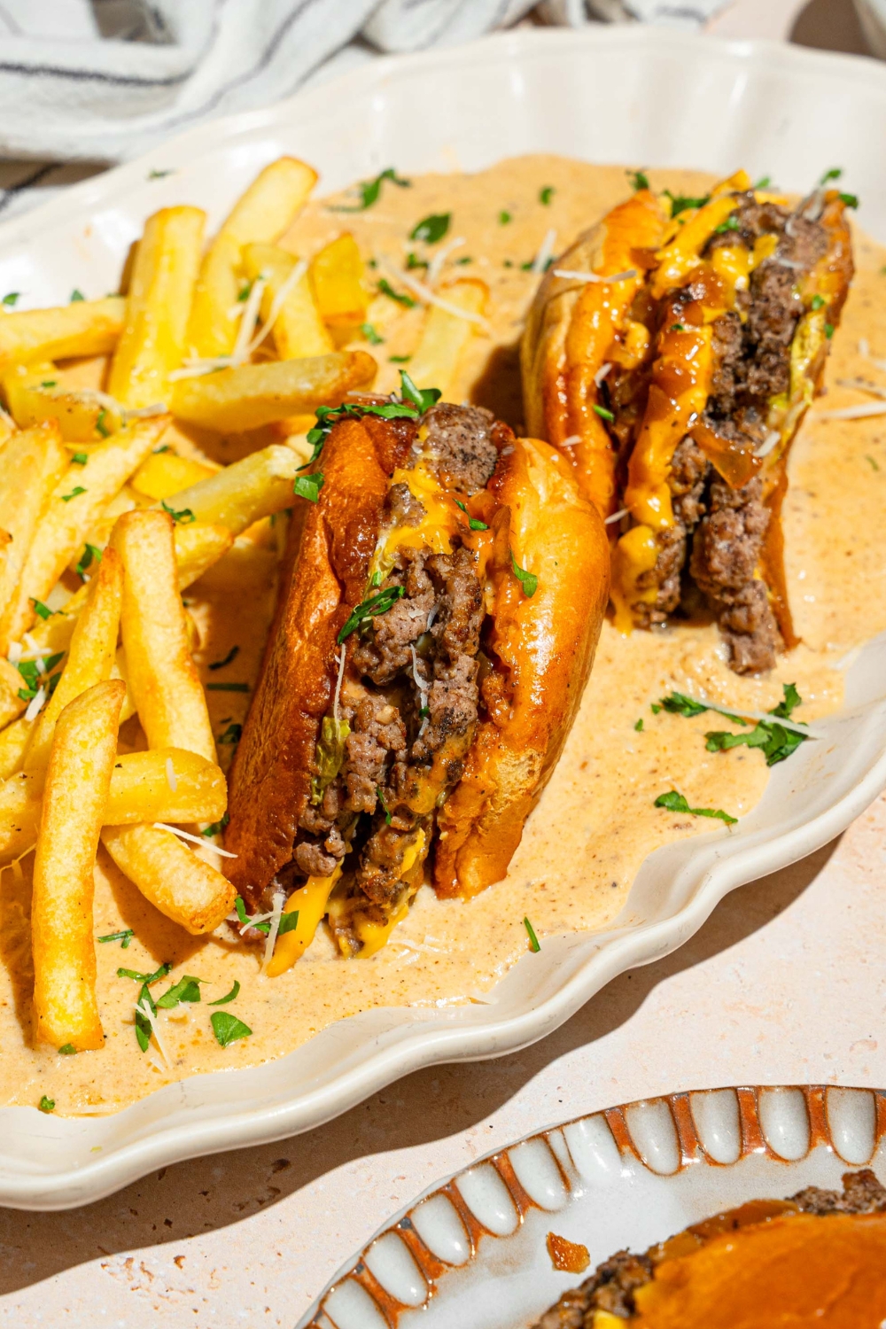 An oval white serving tray with a half of a cheeseburger face down in a creamy garlic Parmesan sauce that is on the plate. Next to the burgers are french fries.