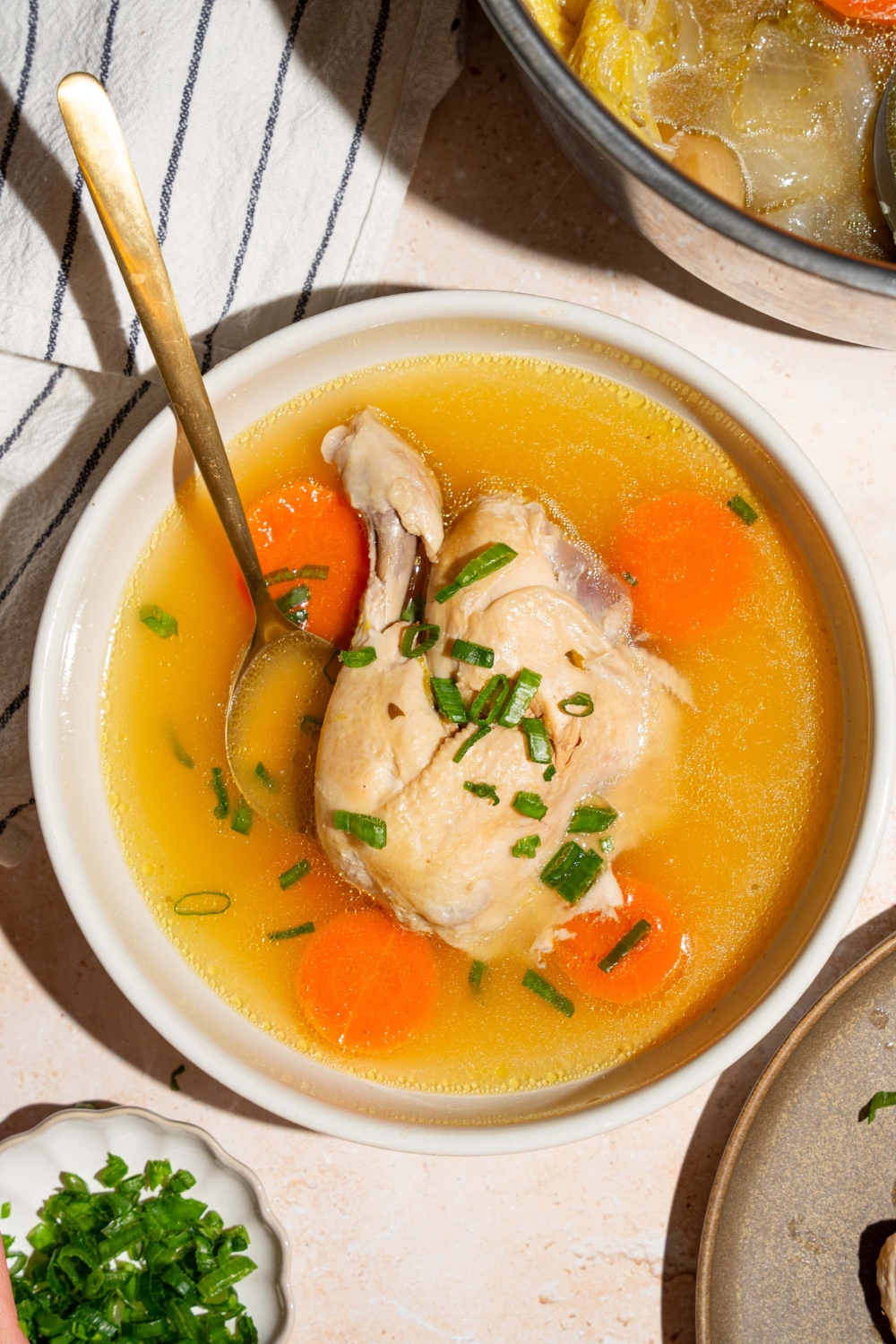 No water chicken soup; part of a whole chicken and carrots in a white bowl with a spoon in it.