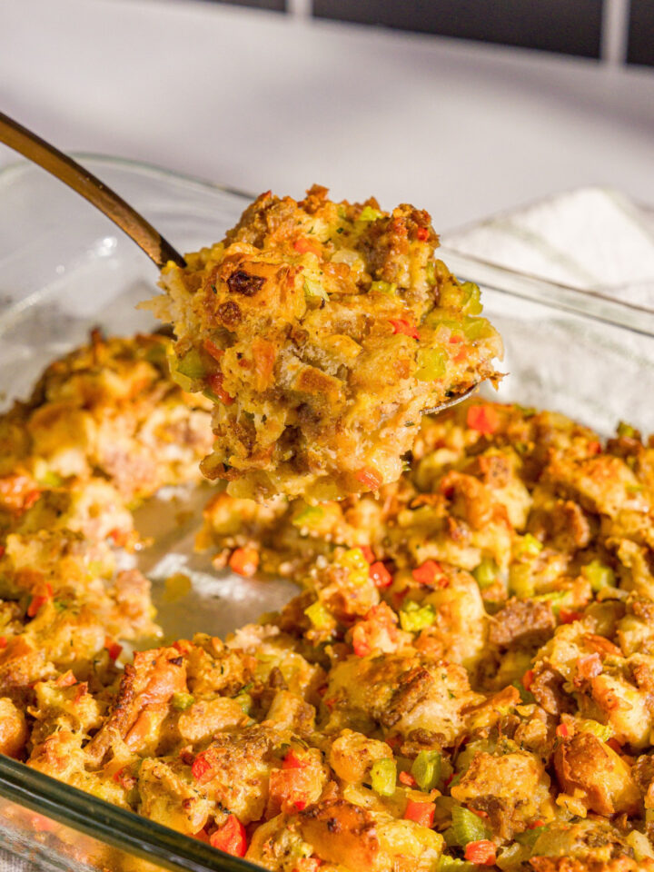 A baking dish of White Castle stuffing with a large spoon taking a scoop of stuffing from the dish. The dish is on a wooden board.