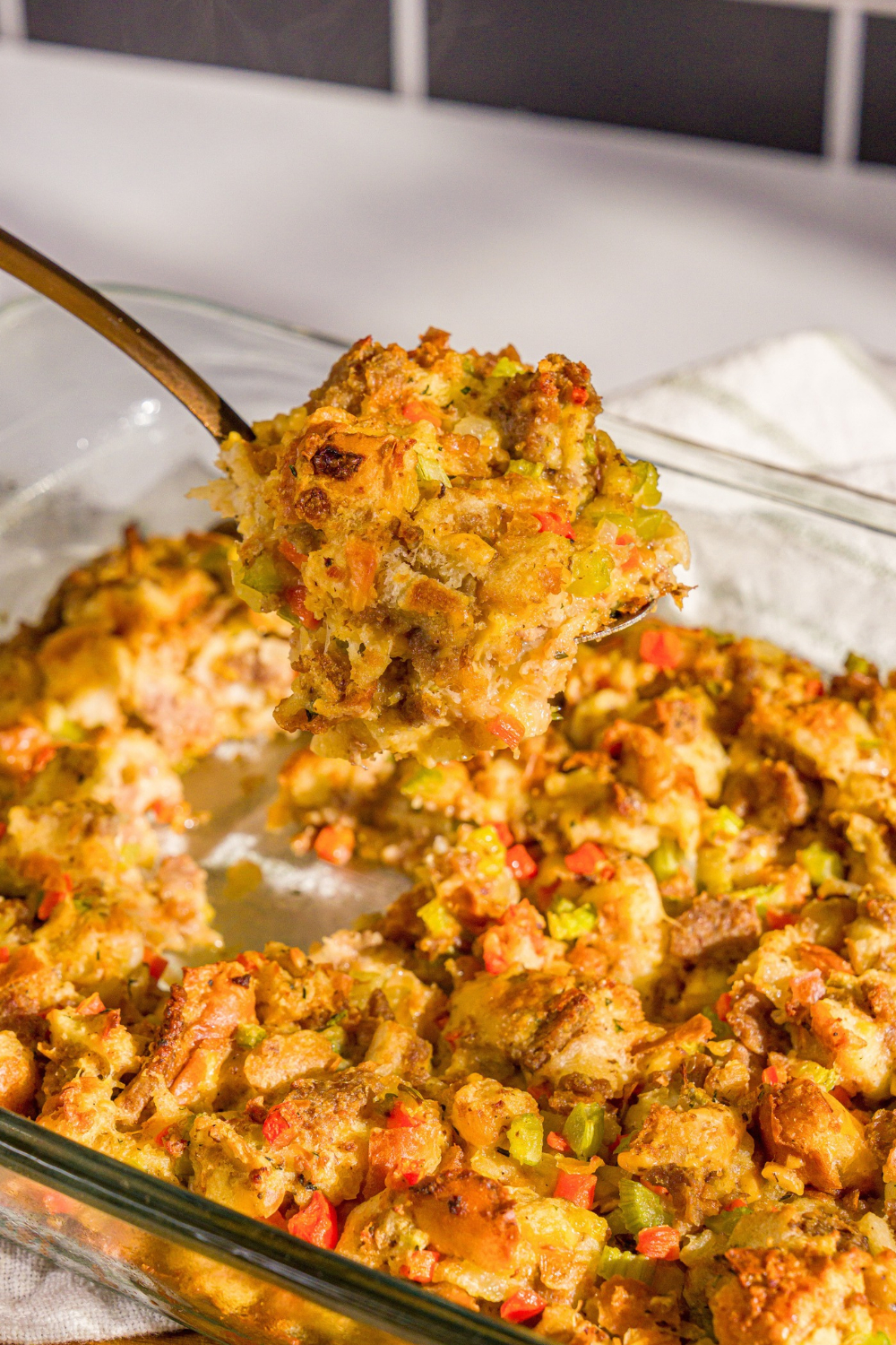 A baking dish of White Castle stuffing with a large spoon taking a scoop of stuffing from the dish. The dish is on a wooden board.